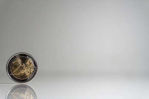 A single 2 Euro coin standing on a reflective surface against a plain background.