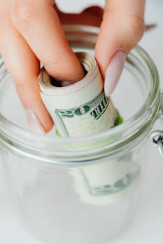 Hand placing rolled US dollars into a glass jar, representing savings and financial planning.